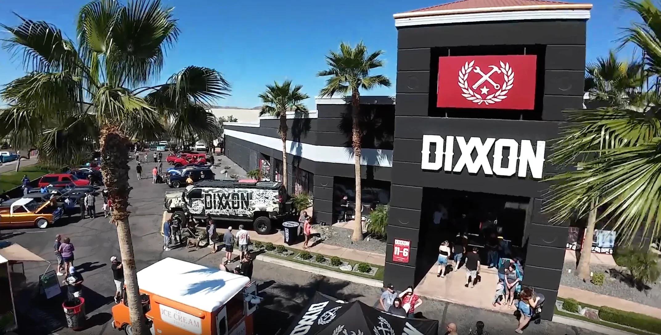 The black Dixxon showroom building under palm trees, with a car show and a crowd in the parking lot.